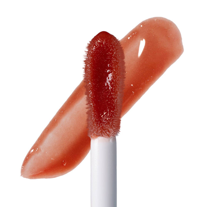 A close-up of a lip gloss applicator with a doefoot tip, positioned over a diagonal swatch of glossy red-brown